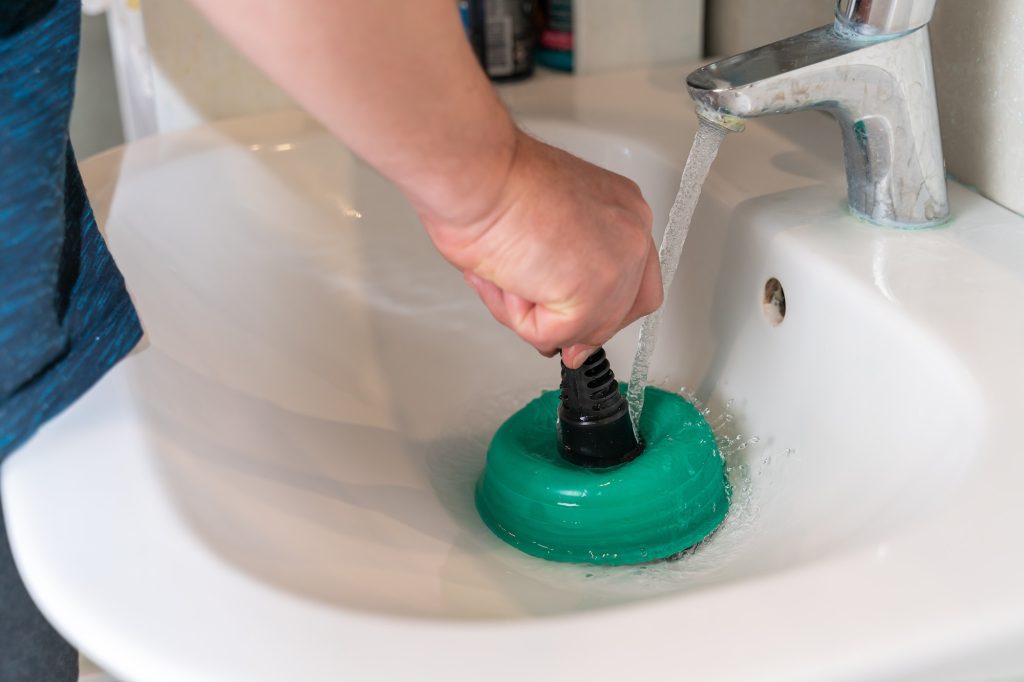 Male hands clean the blockage in the washbasin with a plunger close-up
